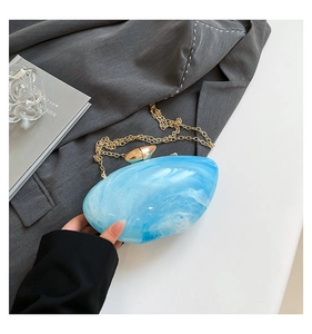 Detail of shell-shaped acrylic evening bag with sky blue marble texture and gold chain