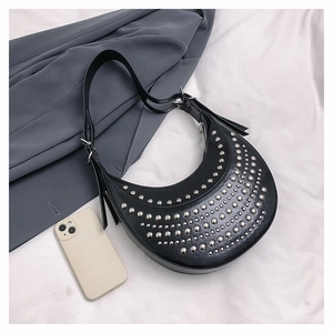 Détail du sac hobo noir en demi-lune avec clous argentés sur fond de tissu blanc