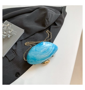 Detail of sea blue marble acrylic shell clutch bag with gold chain on grey fabric