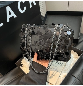 Détail du sac à paillettes noires avec bandoulière chaîne dans un coffret cadeau chic
