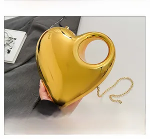 Close-up of heart-shaped gold acrylic evening bag with glossy mirror finish and chain