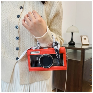 Detail of red camera-shaped handbag with silk scarf handle and silver chain strap
