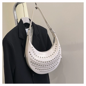 Détail d'un sac demi-lune blanc avec rivets argentés suspendu sur une veste noire