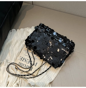 Détail du sac à bandoulière à paillettes noires avec chaîne en cuir sur tissu blanc