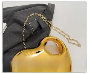 Detail of a shiny gold heart-shaped acrylic evening bag with a metallic chain strap