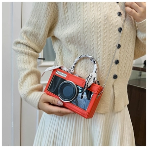 Detail of red camera-shaped bag with crystal lens and scarf-wrapped handle on a model