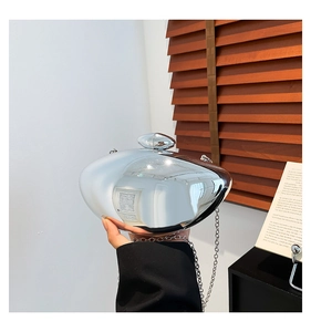 Detail of silver mirror acrylic clutch bag with slender chain strap on a black tray