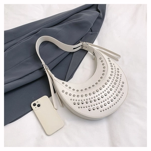 Détail du sac demi-lune en cuir blanc avec clous et un téléphone pour l'échelle