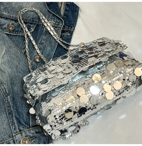 Gros plan du sac bandoulière argenté à paillettes avec chaîne sur fond blanc texturé