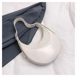 Détail d'un sac demi-lune crème sur une veste grise avec sangle réglable argentée
