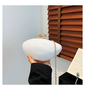 Close-up of white marble acrylic evening clutch bag with gold spherical clasp and chain