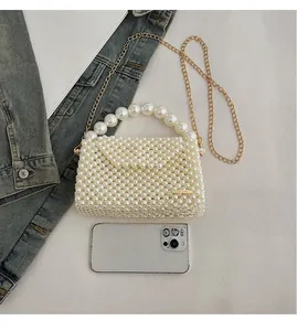 Detailed top view of a handmade pearl woven mini bag with golden metal chain strap