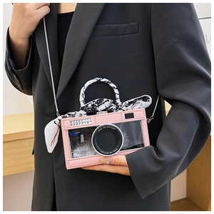 Pink camera-shaped handbag featuring transparent PVC, silk scarf handle, and silver chain