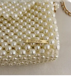 Close-up of white handmade pearl beaded handbag with elegant golden logo plaque detail