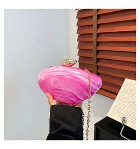 Close-up of pink marble acrylic clutch bag with gold chain strap held by a model