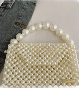 Detailed view of woven pearl handbag with oversized pearl handle and gold metal plate
