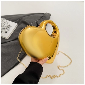 Detail of a shiny gold heart-shaped acrylic handbag with elegant metal chain strap