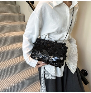 Vue latérale d'un sac bandoulière à paillettes noires avec une chaîne en métal