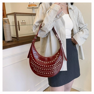 Sac bandoulière demi-lune rouge foncé à clous argentés porté par un mannequin au café