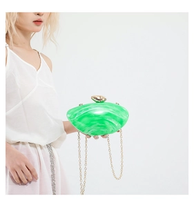 Detail of green acrylic clutch with marble texture and elegant gold chain strap