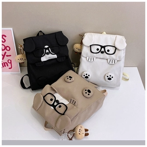Detailed view of three cute cartoon dog backpacks in black, white, and khaki with charms