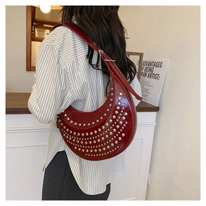 Détail du sac demi-lune en cuir verni rouge avec rivets argentés punk porté à l'épaule