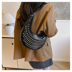 Détails des clous argentés sur le sac croissant noir porté avec un blazer marron