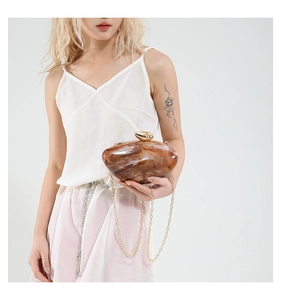 Detail of an acrylic mango shaped evening bag with amber marble pattern and gold chain