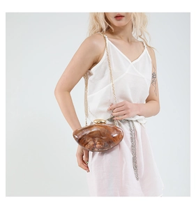 Detail showing amber marble acrylic shell bag with gold chain and spherical metal clasp