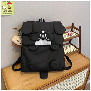 Detail of cute black cartoon dog backpack with 3D ears and plush pendant on wood table