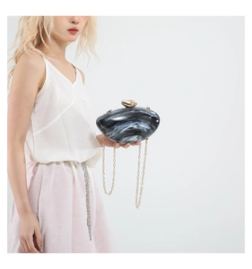 Detail of marble pattern acrylic clutch with gold chain strap worn by a model