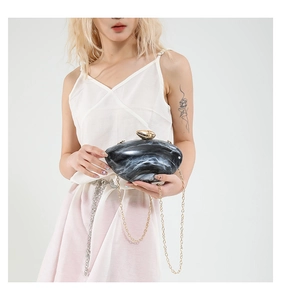 Close-up of marble acrylic clutch bag with golden shell lock on model