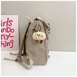 Detailed side view of beige nylon backpack with large capacity and cute plush pendant charm
