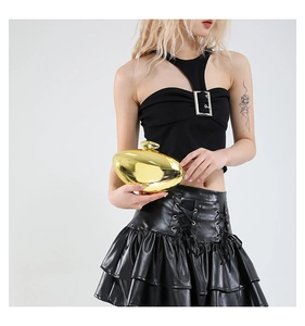 Close-up of golden pebble-shaped acrylic evening bag held by a model in black outfit