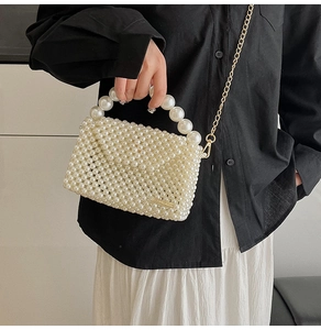 Detailed close-up of woven cream pearl handbag with golden metal logo and chain strap