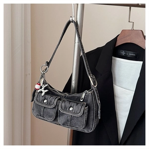 Close-up of denim shoulder bag featuring utility pockets and a silver balloon dog charm