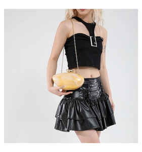 Detail of yellow marble texture acrylic clutch bag with golden chain on model's shoulder