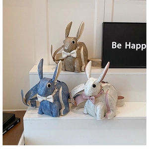 Three cute bunny crossbody bags in gold, blue, and white arranged on a display stand