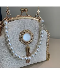 Detail of cream leather shell bag with pearl handle, gold tassel, and metal clasp