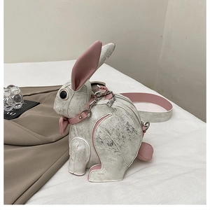 Detail of bunny cross-body bag featuring pink bow and silver chain on soft bedding