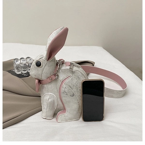 Detailed side view of rabbit-shaped crossbody bag with pink strap next to phone