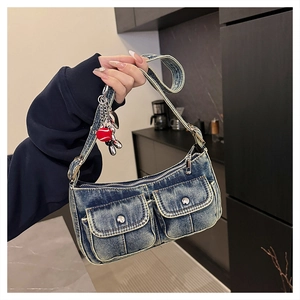 Detail of blue denim hobo bag with front flap pockets and a red balloon dog charm