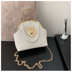 Close-up of retro cream shell bag with pearl handle and golden heart emblem detail