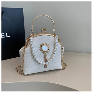 Detail of cream-colored shell bag with pearl decor, gold handle and metal chain