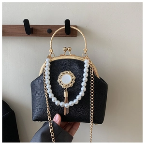 Close-up of black lychee leather bag with pearl strap, gold metal handle and tassel