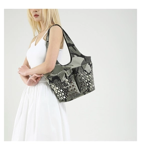 Detail of camouflage canvas shoulder bag with silver rivet studs on a white dress model