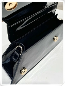 Detail of minimalist black patent leather handbag featuring dual magnetic snap closures