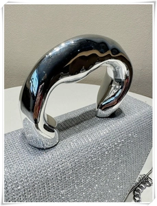 Detail of silver glitter handbag featuring a thick metallic curved handle and chain strap