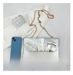 Pochette plissée argentée avec chaîne dorée présentée à côté d'un smartphone