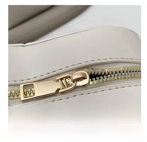 Détail macro montrant la fermeture éclair dorée lisse et la couture sur le sac en cuir blanc